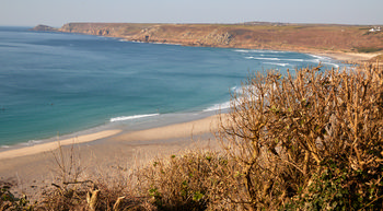 Sennen cove This landscape photograph shows Sennen Cove, a well-known beach located on the coast of Cornwall, United Kingdom. The image was captured in the late afternoon during early spring, as evidenced by the soft lighting and the clear sky. The view overlooks the curve of the cove, with gentle waves approaching the sandy beach, and the rugged, natural coastline of Cornwall extending into the distance. The foreground features coastal vegetation, adding to the scene's emphasis on nature. Sennen Cove is a popular destination in Cornwall for its scenic coastline, and the image highlights both the expansive beach and the surrounding natural environment typical of the United Kingdom's south-west shores.